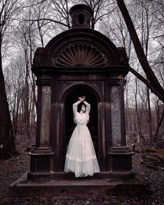 a woman in a white dress is standing at the entrance to a cemetery with her hands on her head