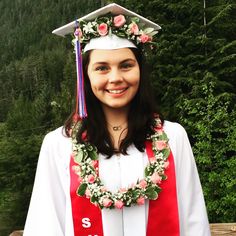 a woman wearing a graduation cap and gown with flowers around her neck is smiling at the camera