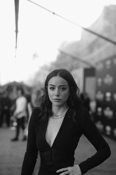 a woman in a black dress standing on the street with her hands on her hips