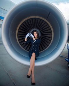 a woman is posing in front of an airplane engine