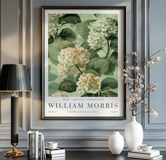 there is a vase with flowers on the table in front of a framed poster that says william morris