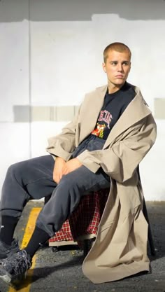 a man sitting on top of a chair next to a white wall and wearing a coat