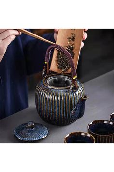 a person holding a wooden stick near a teapot and other items on a table