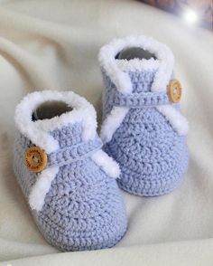 a pair of blue crocheted baby booties with buttons on them sitting on a bed