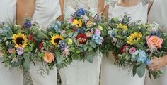 four bridesmaids in white dresses holding bouquets of sunflowers and greenery