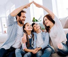 a family is sitting on the floor making a heart shape with their hands and smiling