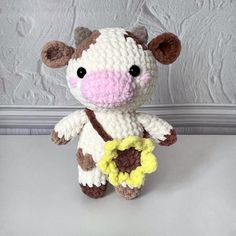 a crocheted stuffed cow holding a flower