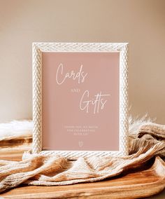 a pink card and gifts sign sitting on top of a wooden table next to a blanket