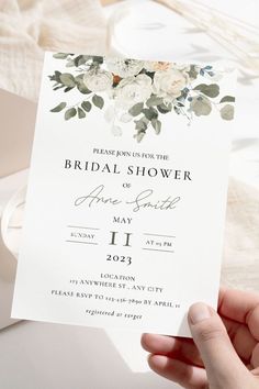 a person holding up a white wedding card with flowers on the front and back side