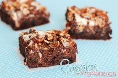 four pieces of chocolate brownie with nuts and cream on top, sitting on a blue surface