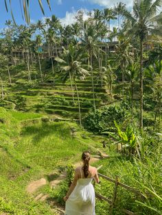 a woman in a white dress is walking down a path with palm trees on the side