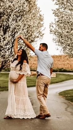 a man and woman dancing in the middle of a road with trees lining both sides