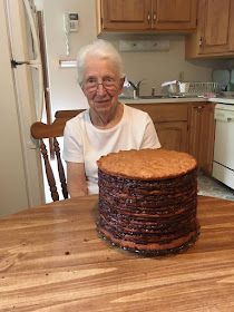 an older woman sitting at a kitchen table with a chocolate cake on top of it