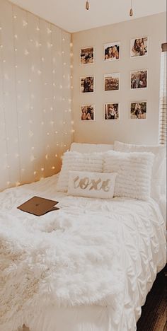 a white bed topped with pillows and blankets next to a wall covered in pictures on it