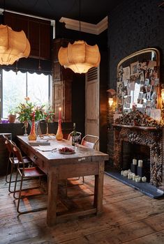 a dining room table and chairs with lights hanging from the ceiling over it, in front of a fireplace