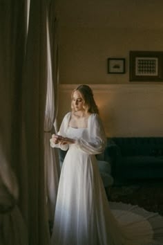 a woman standing in front of a window wearing a white dress