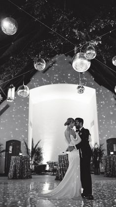 a bride and groom standing in front of a large white building with disco balls hanging from the ceiling