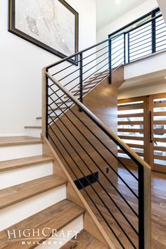 a wooden staircase with metal handrails in a modern style home, which features hardwood floors and white walls