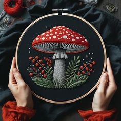 two hands are holding up a cross - stitch project with mushrooms and berries on it