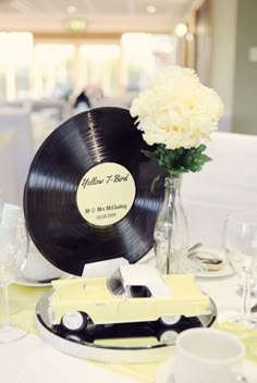 a table topped with a black record and white car next to a vase filled with flowers