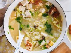 a bowl of soup with tofu and broccoli in it on a table