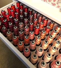 many spools of thread are sitting in a drawer next to each other on the table