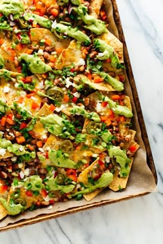 nachos with guacamole, tomatoes and other toppings on a tray