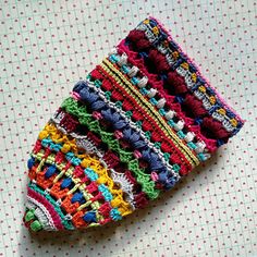 a crocheted piece of cloth on top of a white tablecloth with red, green, yellow and blue stripes