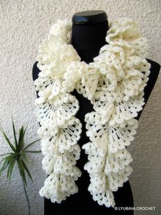 a white crocheted scarf on a mannequin next to a potted plant