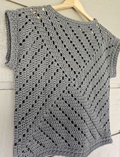 a gray crocheted sweater hanging on a wooden hanger next to a white wall