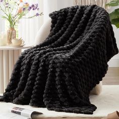 a black knitted blanket sitting on top of a white rug next to a chair