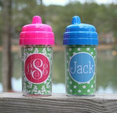 two personalized sippy cups sitting next to each other on a wooden table with water and trees in the background