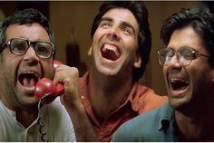 three men are laughing and one is on the phone while another man holds his mouth open