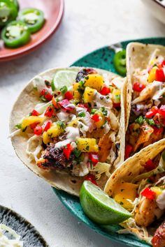 three tacos with chicken, pineapple salsa and lime wedges on a plate