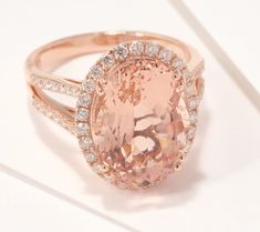 an oval shaped pink stone surrounded by white diamonds in a rose gold ring on a white surface