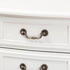 a white dresser with two drawers and handles on each drawer, one has an ornate handle