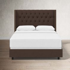 a bed with white sheets and brown headboard in a room that has hardwood floors