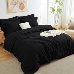 a bed with black sheets and pillows in a room next to a painting on the wall