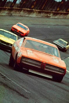 an orange car driving down a race track with other cars behind it in the background