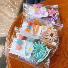 three clear plastic bags filled with assorted hair accessories on top of a wooden table