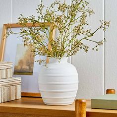 a white vase filled with flowers sitting on top of a wooden table next to books