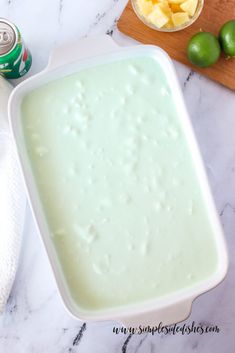 a white dish filled with green liquid next to limes and a can of soda