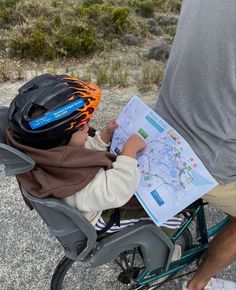 a young boy sitting on top of a bike while holding a map