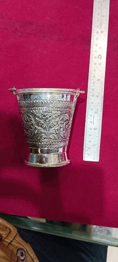 a silver cup sitting on top of a table next to a ruler and glove holder