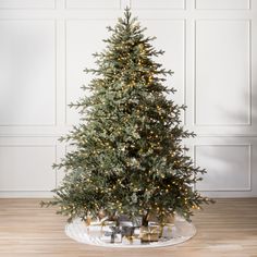 a christmas tree with presents under it on a wooden floor in front of a white wall