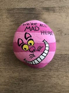 a pink rock with the words we're all mad here painted on it and an image of a cat