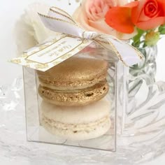 three macaroons in a clear box with a ribbon around the edge and flowers behind it