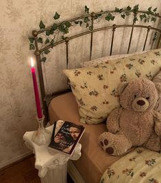 a brown teddy bear sitting on top of a bed next to a book and candle