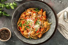 a bowl filled with pasta and chicken on top of a table next to some spices