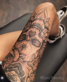 a woman's leg with a skull and flowers tattoo on her arm, sitting in a chair